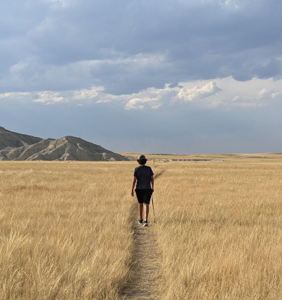 A photo of a young person hiking on a prairie towards hills in the background